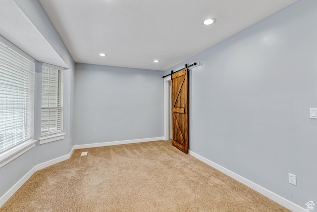spare room with light carpet, recessed lighting, baseboards, and a barn door
