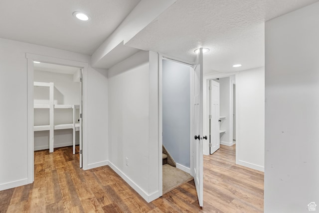 hall featuring light wood-type flooring, recessed lighting, baseboards, and a textured ceiling