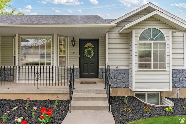 entrance to property featuring stone siding, roof with shingles, and a porch