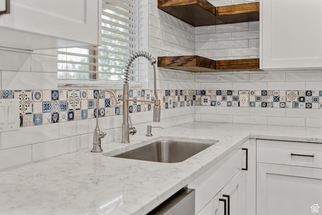 kitchen featuring a sink, decorative backsplash, white cabinets, and light stone counters