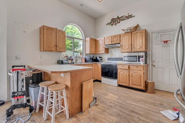 kitchen featuring stainless steel appliances, a peninsula, high vaulted ceiling, a breakfast bar area, and light wood-style flooring