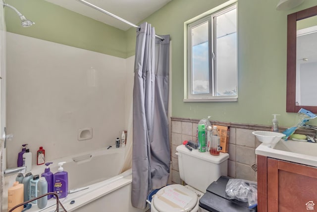 full bath with tile walls, shower / bath combination with curtain, toilet, vanity, and a wainscoted wall