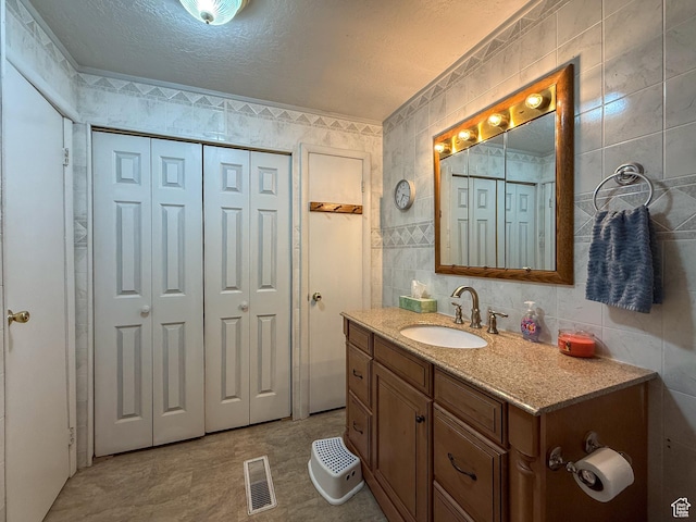 bathroom featuring a closet, tile walls, vanity, and a textured ceiling