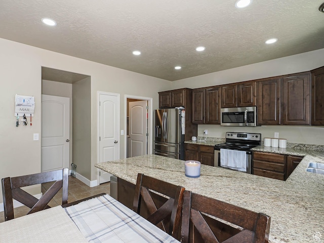 3263 W Blue Moon Ln, South Jordan, UT 84095 - kitchen with stainless steel appliances, dark brown cabinetry, baseboards, a textured ceiling, and a kitchen breakfast bar