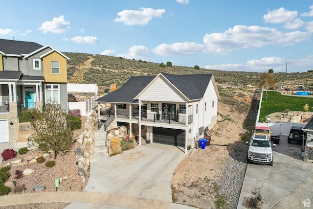 view of front of property with an attached garage, a balcony, concrete driveway, stairway, and stone siding
