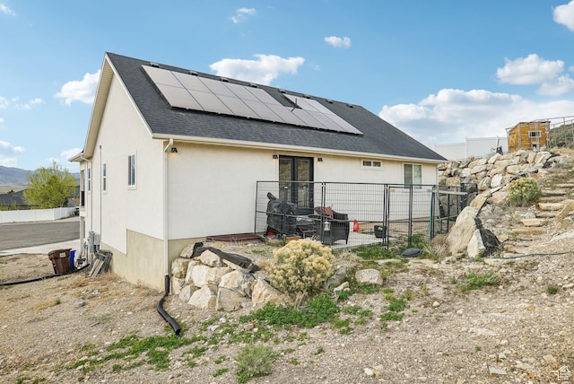 back of house featuring roof mounted solar panels, stucco siding, a shingled roof, and fence