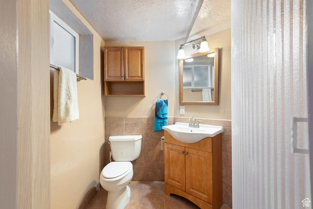 bathroom featuring a textured ceiling, tile walls, toilet, tile patterned floors, and vanity