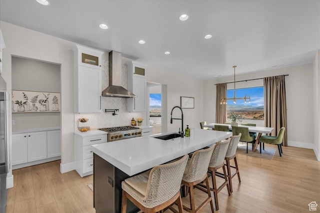 1003 N Grand Heights Dr, St George, UT 84770 - kitchen featuring wall chimney range hood, a sink, decorative backsplash, a kitchen island with sink, and light countertops