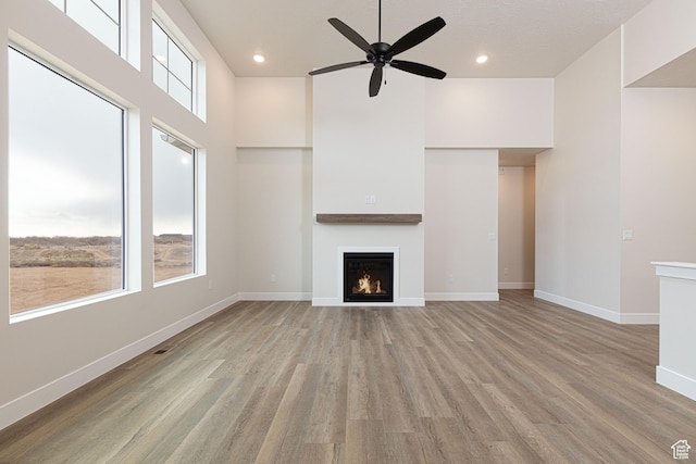 unfurnished living room featuring a warm lit fireplace, a ceiling fan, light wood-style flooring, baseboards, and recessed lighting