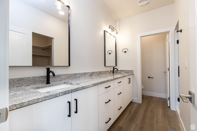 bathroom with wood finished floors, toilet, double vanity, and baseboards
