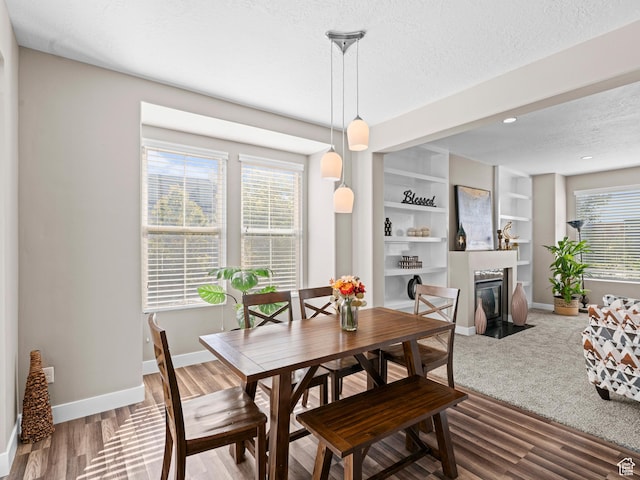 dining area featuring a textured ceiling, baseboards, a fireplace with flush hearth, built in features, and wood finished floors