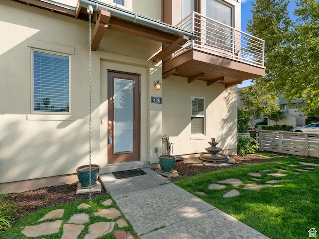 doorway to property with a balcony, fence, and stucco siding