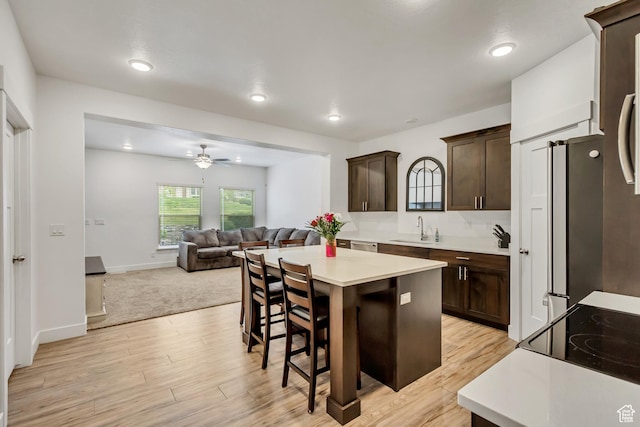 kitchen with a sink, dark brown cabinetry, ceiling fan, light countertops, and a kitchen breakfast bar