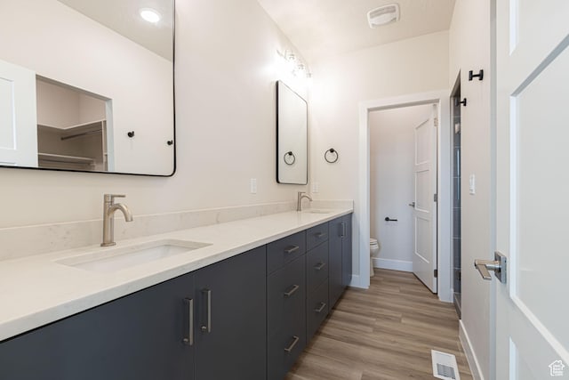 full bathroom with toilet, double vanity, wood finished floors, and baseboards