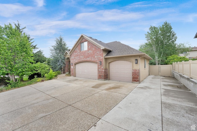 view of side of home with concrete driveway, fence, a shingled roof, brick siding, and a garage