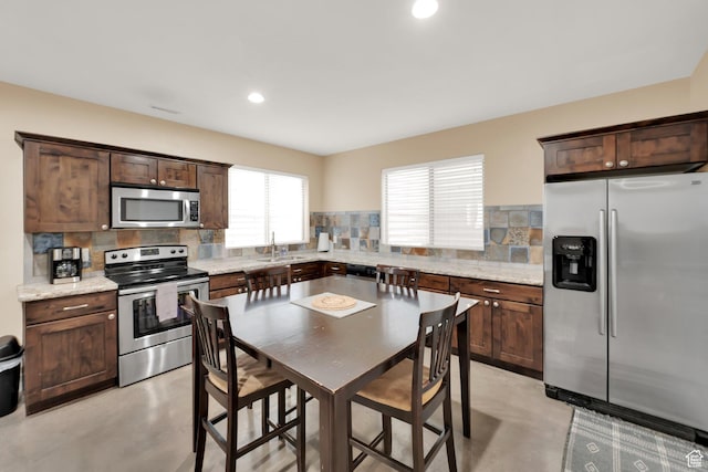 kitchen with appliances with stainless steel finishes, finished concrete floors, backsplash, dark brown cabinets, and a sink