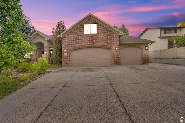 traditional home featuring brick siding, concrete driveway, an attached garage, and fence