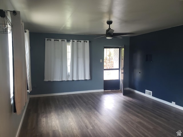 empty room with dark wood-style flooring, a ceiling fan, and baseboards