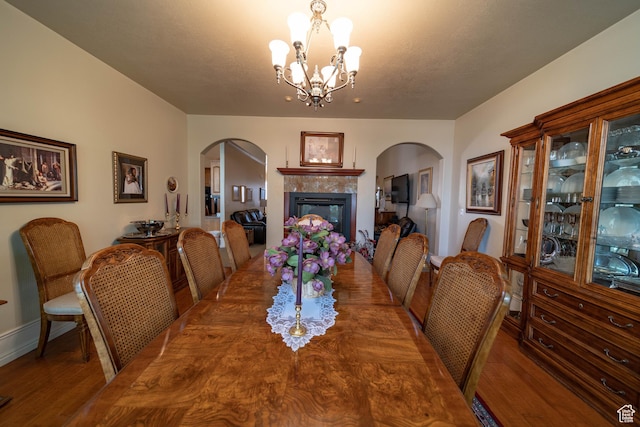 dining area featuring arched walkways, wood finished floors, a chandelier, and a tile fireplace