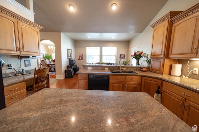 kitchen featuring black dishwasher, a sink, wood finished floors, arched walkways, and backsplash