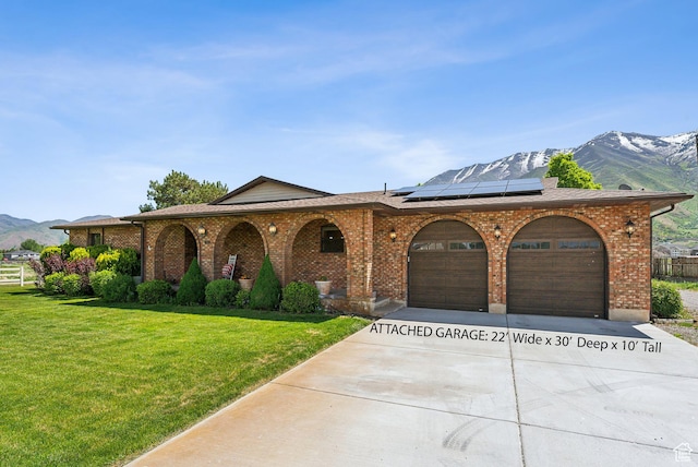 view of front of house with a mountain view, an attached garage, concrete driveway, a front lawn, and roof mounted solar panels