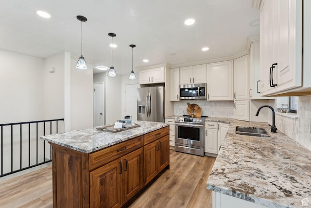 kitchen with appliances with stainless steel finishes, a sink, light wood finished floors, light stone counters, and recessed lighting