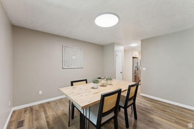 dining space featuring light wood finished floors, baseboards, and a textured ceiling