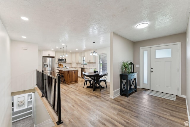 foyer entrance featuring light wood-type flooring, baseboards, a textured ceiling, and recessed lighting