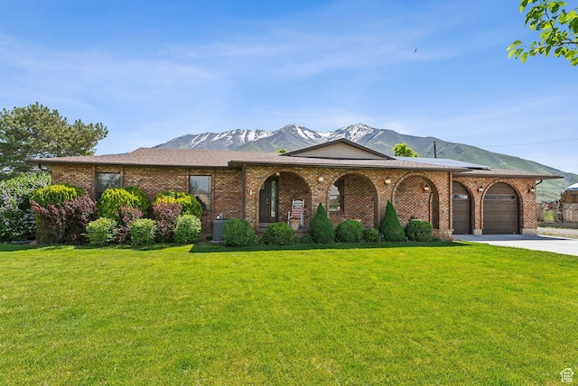 view of front facade featuring a mountain view, a front lawn, an attached garage, and driveway