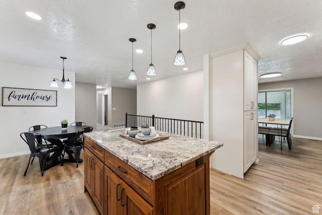 kitchen featuring brown cabinets, light wood finished floors, decorative light fixtures, a center island, and recessed lighting