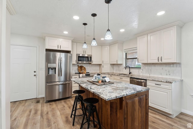 kitchen with appliances with stainless steel finishes, a sink, light wood-style floors, a kitchen island, and backsplash