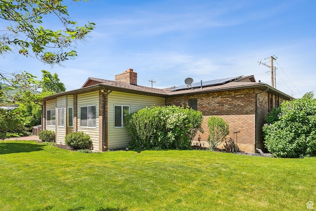 view of side of home featuring a chimney, a yard, roof mounted solar panels, and brick siding