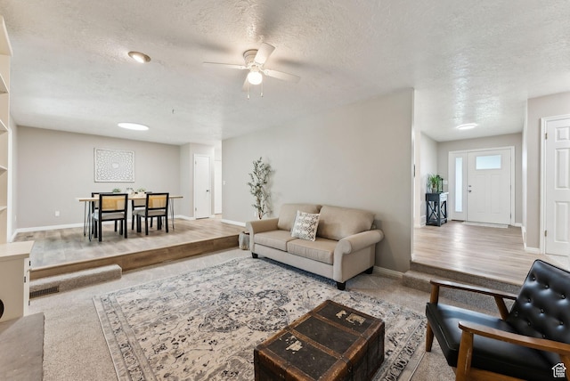 carpeted living room featuring ceiling fan, a textured ceiling, and baseboards