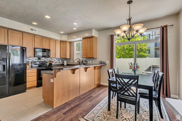 6297 W Traveler Ln, West Jordan, UT 84081 - kitchen featuring black appliances, a textured ceiling, a kitchen breakfast bar, a chandelier, and light wood-style floors