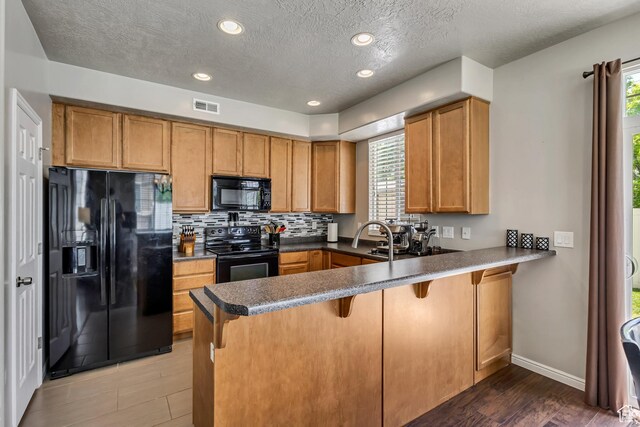 6297 W Traveler Ln, West Jordan, UT 84081 - kitchen with black appliances, a peninsula, plenty of natural light, brown cabinets, and a textured ceiling