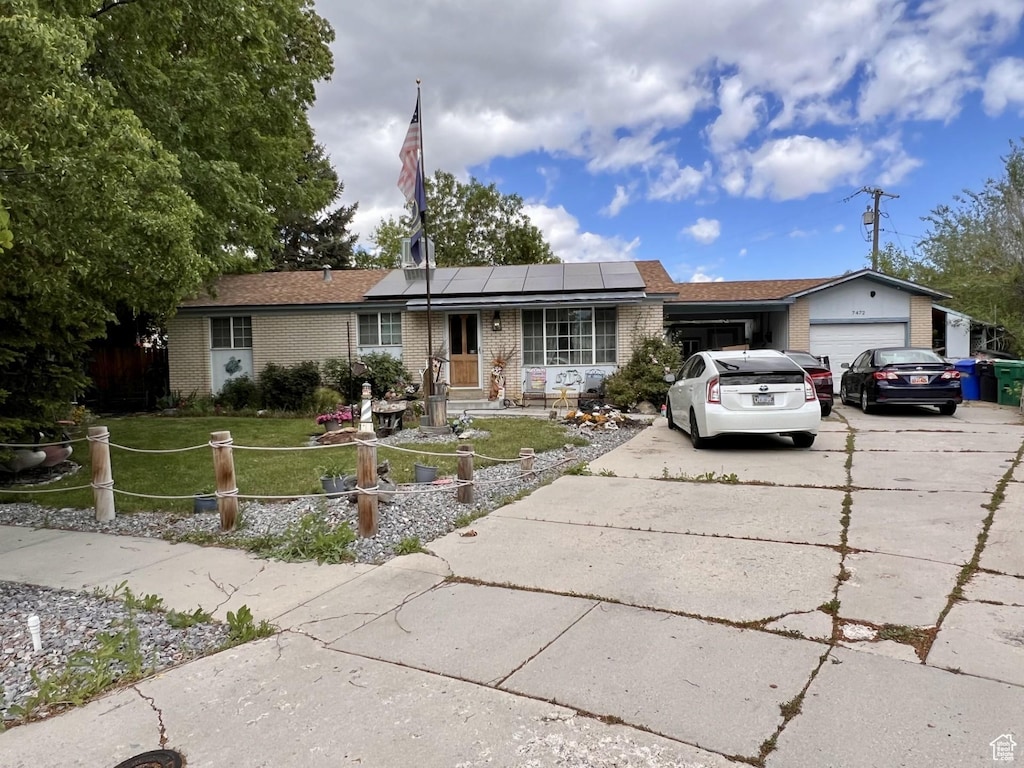 ranch-style house with a front yard, brick siding, a garage, and roof mounted solar panels