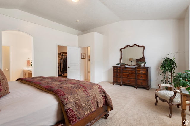 bedroom with lofted ceiling, light carpet, ensuite bathroom, a spacious closet, and baseboards