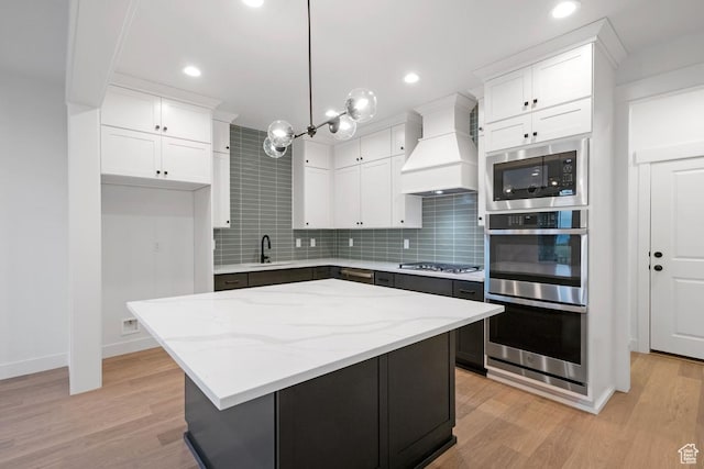 kitchen featuring appliances with stainless steel finishes, a sink, custom range hood, white cabinetry, and backsplash