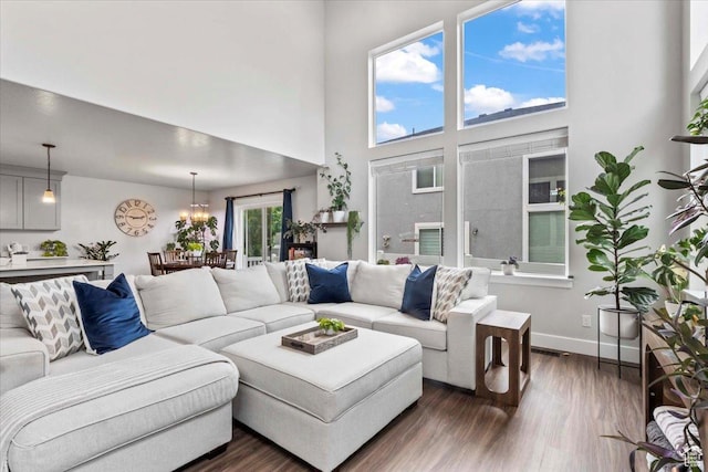living area with dark wood finished floors, a chandelier, a high ceiling, and baseboards