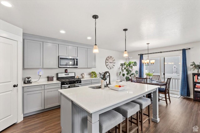 kitchen with a sink, stainless steel appliances, gray cabinets, a breakfast bar area, and dark wood finished floors