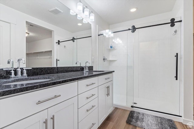 full bath featuring a shower stall, wood finished floors, double vanity, and recessed lighting