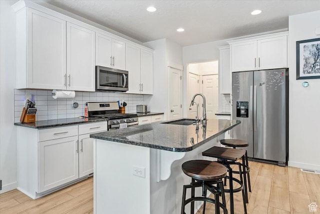 kitchen with stainless steel appliances, a sink, light wood-style flooring, white cabinetry, and backsplash