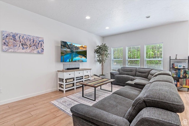 living room featuring light wood-type flooring, a textured ceiling, recessed lighting, and baseboards