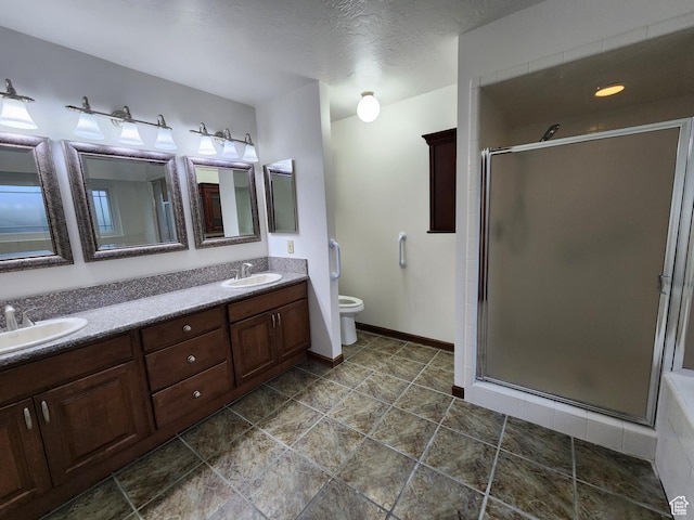 bathroom with a stall shower, double vanity, toilet, and baseboards
