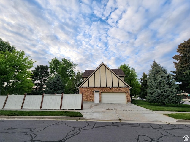 tudor house featuring brick siding, driveway, fence, and a garage