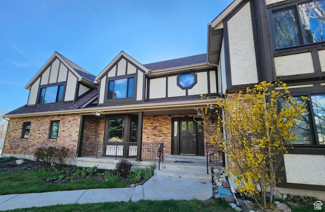 tudor-style house featuring covered porch, stucco siding, and brick siding
