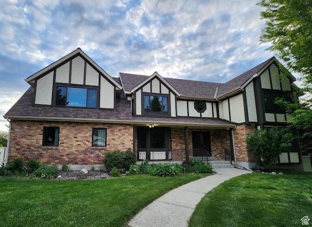 english style home with covered porch, a front lawn, stucco siding, and brick siding