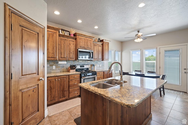 607 N 1980 E Unit 139, Spanish Fork, UT 84660 - kitchen with appliances with stainless steel finishes, a sink, a textured ceiling, brown cabinets, and a kitchen island with sink