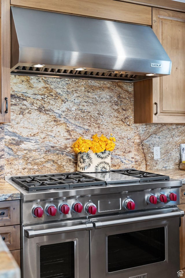 kitchen with wall chimney exhaust hood, double oven range, and decorative backsplash