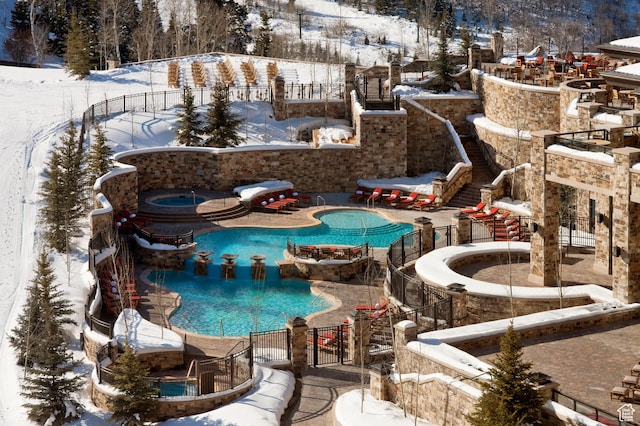 snow covered pool featuring a hot tub, a community pool, a patio area, and fence